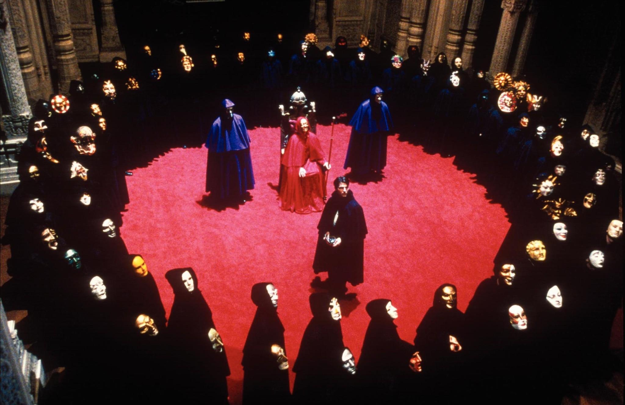 Image from film, Eyes Wide Shut. A man stands unmasked and exposed before a group of Cultists in robes and masquerade masks.